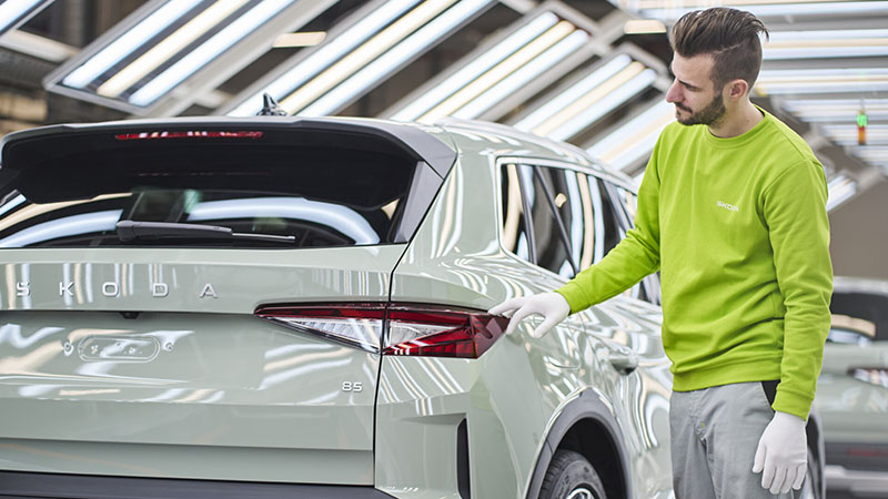 Pracovník Škoda v zářivě zelené uniformě kontroluje zadní světlo SUV na lince